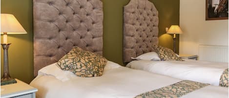 A hotel room with two beds, each with a tufted headboard, white bedding, patterned pillows, and bedside lamps.