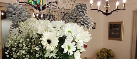 A vase with white flowers and pinecones on a table in a room with a chandelier and framed pictures on the wall.