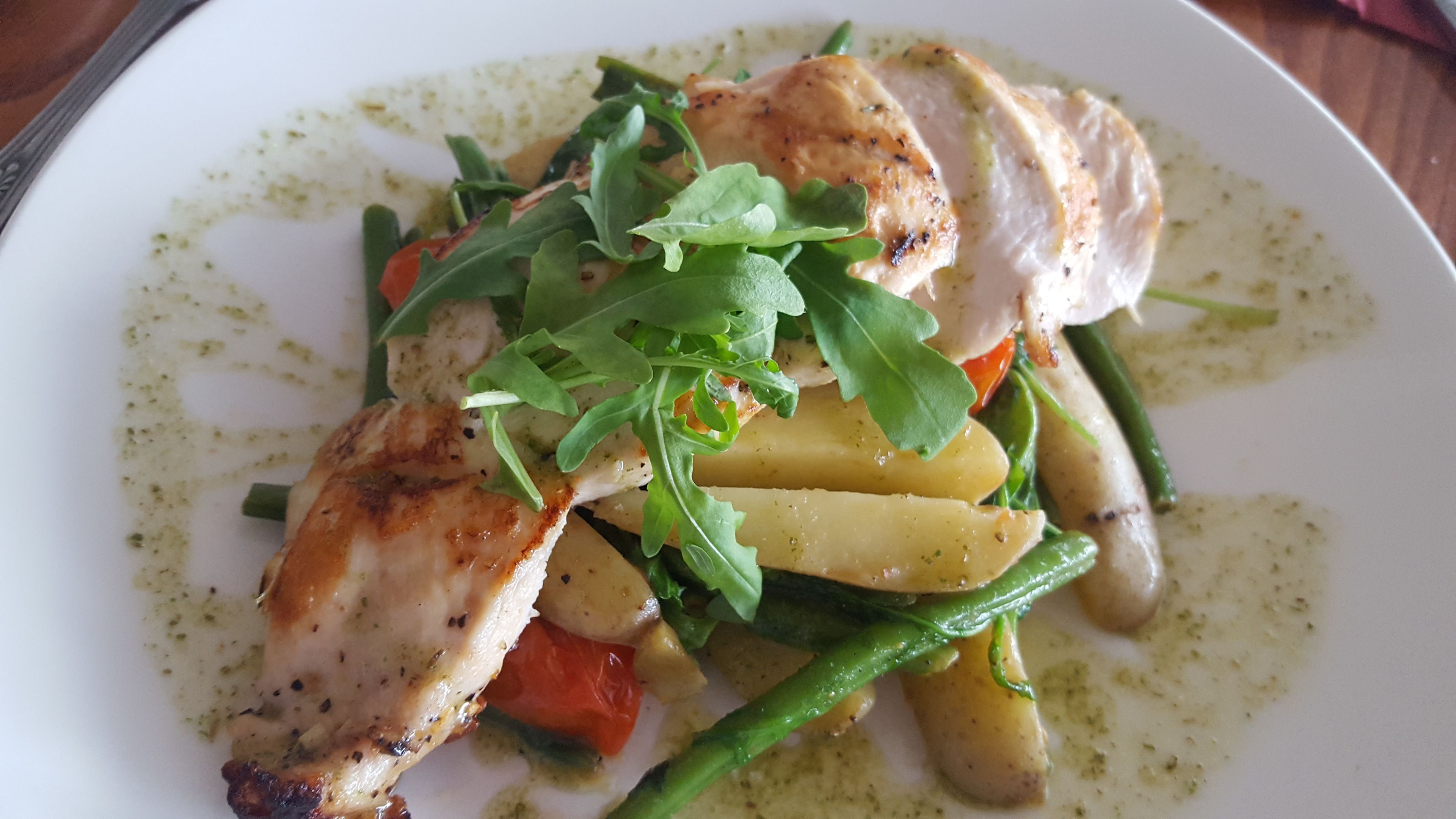 A plate of food with chicken, vegetables, and a green sauce.