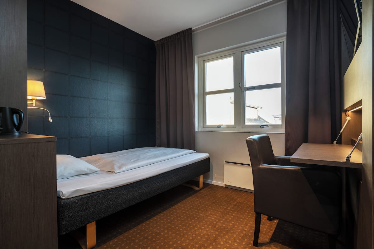 Habitación de hotel con cama, escritorio, silla, lámpara y ventana con cortinas.