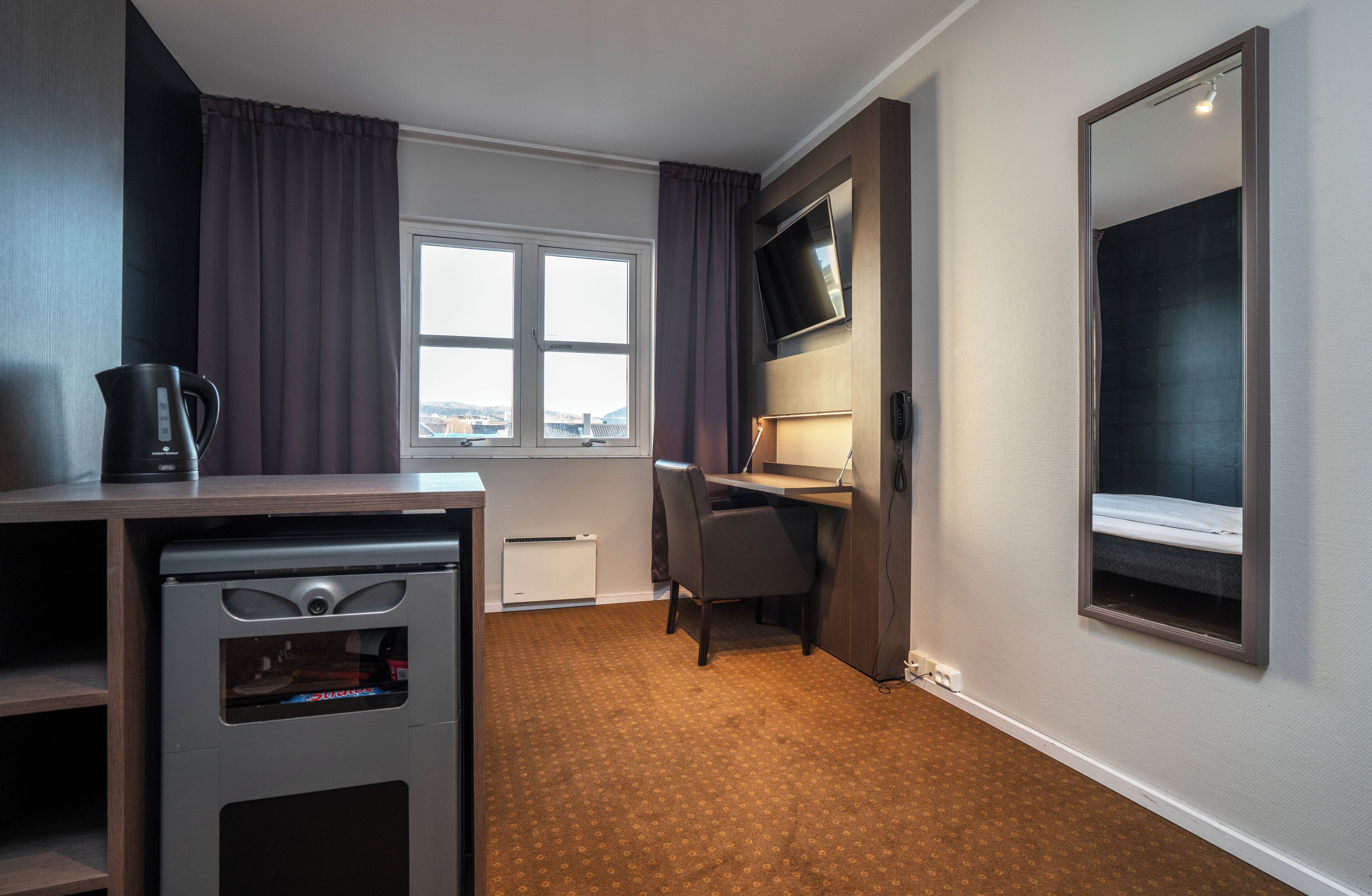Habitación de hotel pequeña con escritorio, silla y un espejo grande.