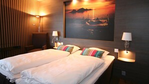 Quarto de hotel com duas camas, uma grande pintura na parede retratando um pôr do sol e duas luminárias de cabeceira.