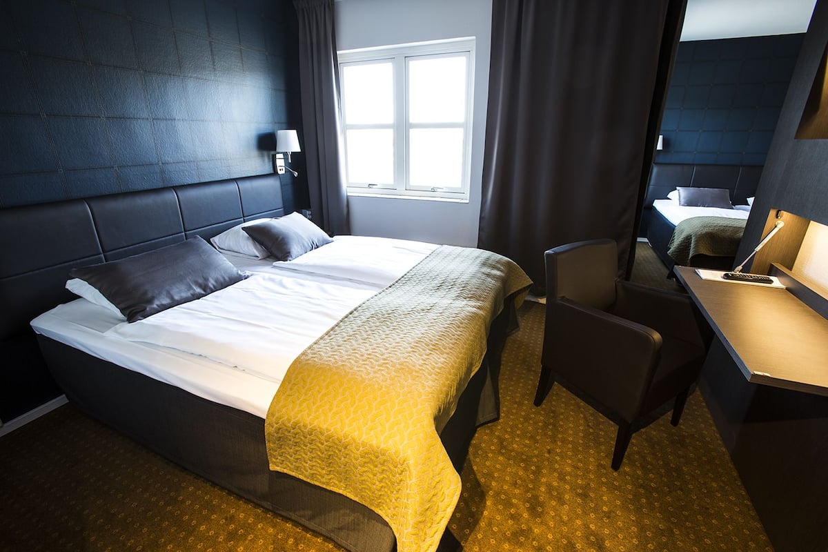 Una habitación de hotel con una cama grande, un escritorio con lámpara y una ventana con cortinas.