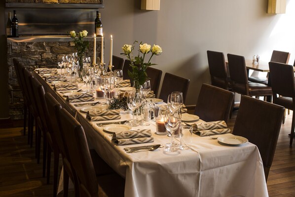 A long dining table set with white tablecloths, candles, and wine glasses, surrounded by chairs.