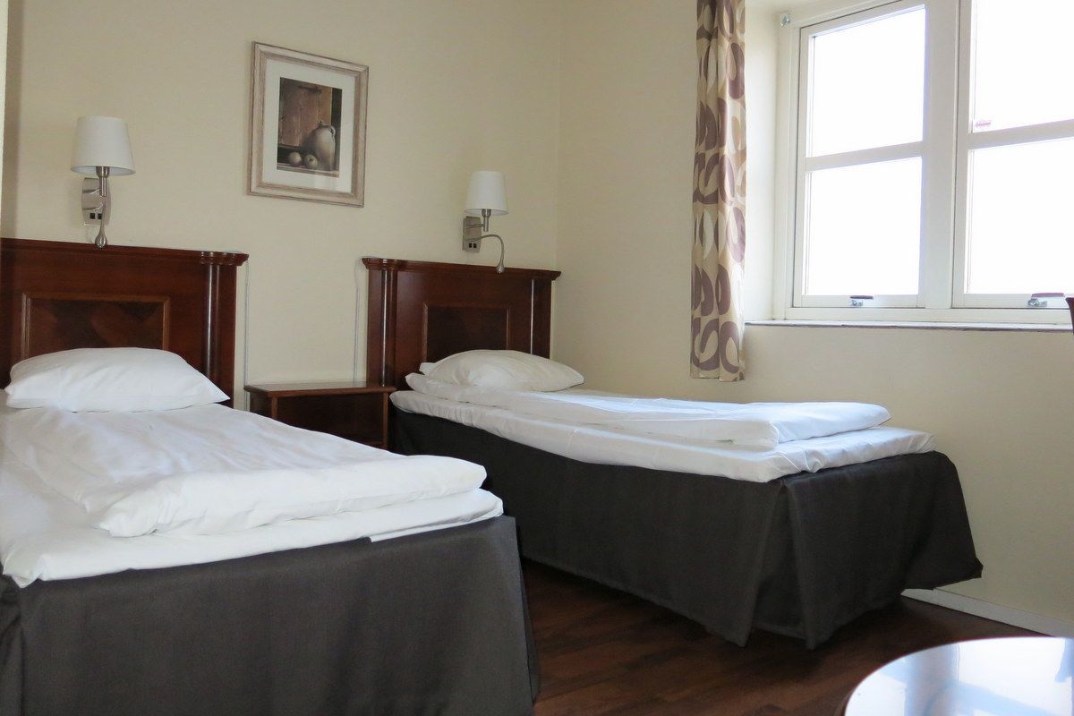 A hotel room with two beds, a small table, a nightstand, and a window with curtains.