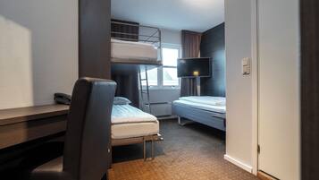 Ett litet hotellrum med en våningssäng, ett skrivbord med en stol, en tv och ett fönster med gardiner.