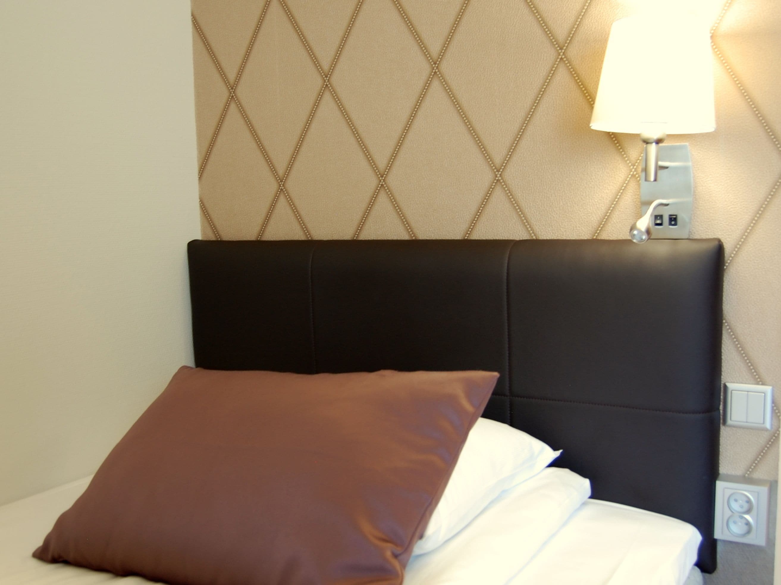 A bed with a black headboard, a brown pillow, and a white bedsheet.