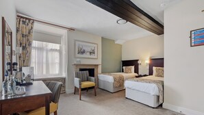 Habitación de hotel con dos camas, un escritorio, una silla, una chimenea y una ventana con cortinas.