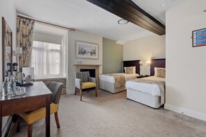 A hotel room with two beds, a desk, a chair, a fireplace, and a window with curtains. - Sleeping Bear Hotel Dorchester (Dorchester)
