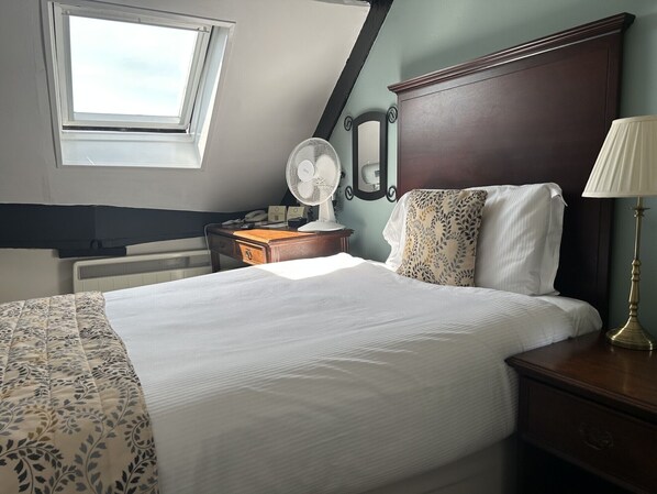 Une chambre d’hôtel équipée d’un lit, d’une table de chevet, d’une lampe et d’un bureau avec un téléphone et un ventilateur.