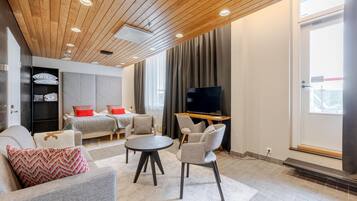 Una sala de estar moderna con sofá, sillas, una mesa redonda, televisor y una cama con cortinas.