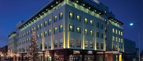 A multi-story hotel with illuminated signage, a Christmas tree, and a street with light trails.
