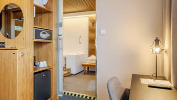 A hotel room with a wooden wardrobe, a desk with a lamp, and a sliding door leading to a bathroom.
