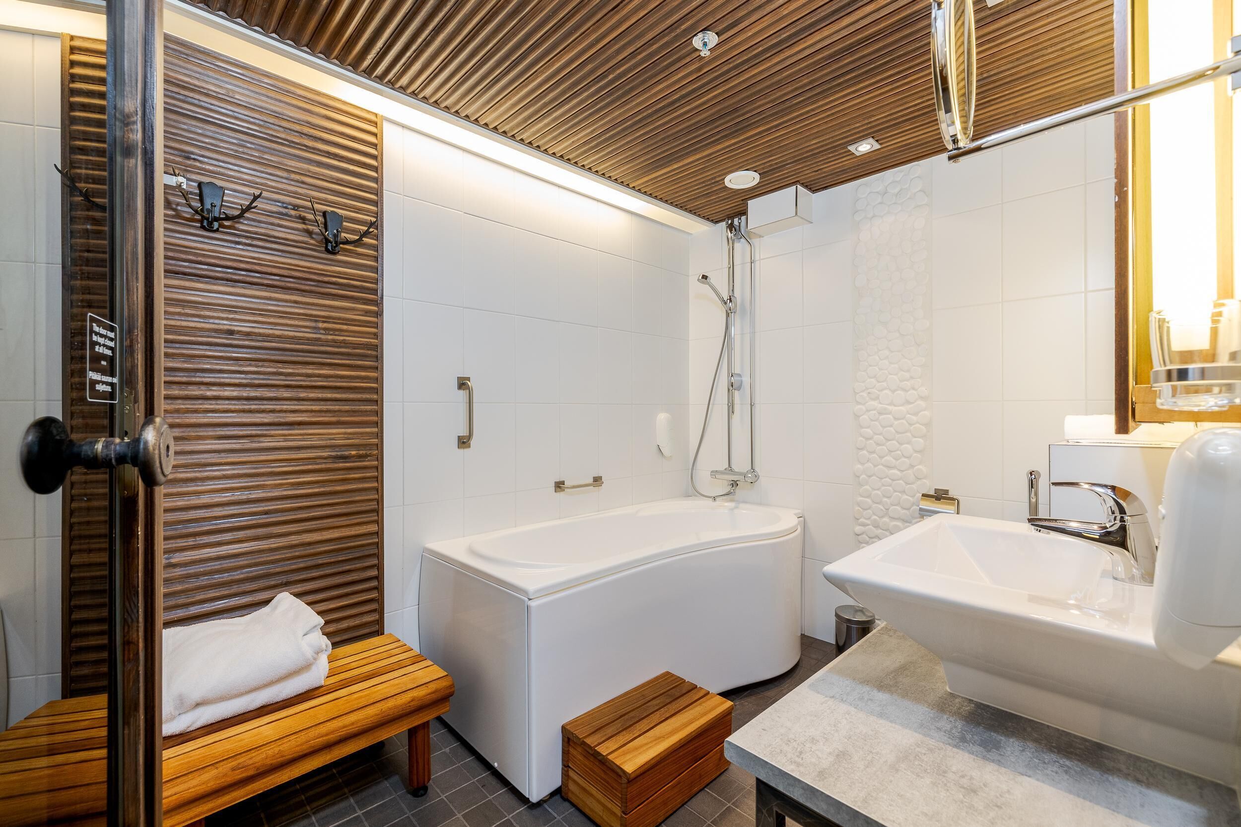 Un baño moderno con una banca de madera, una bañera y un lavamanos.