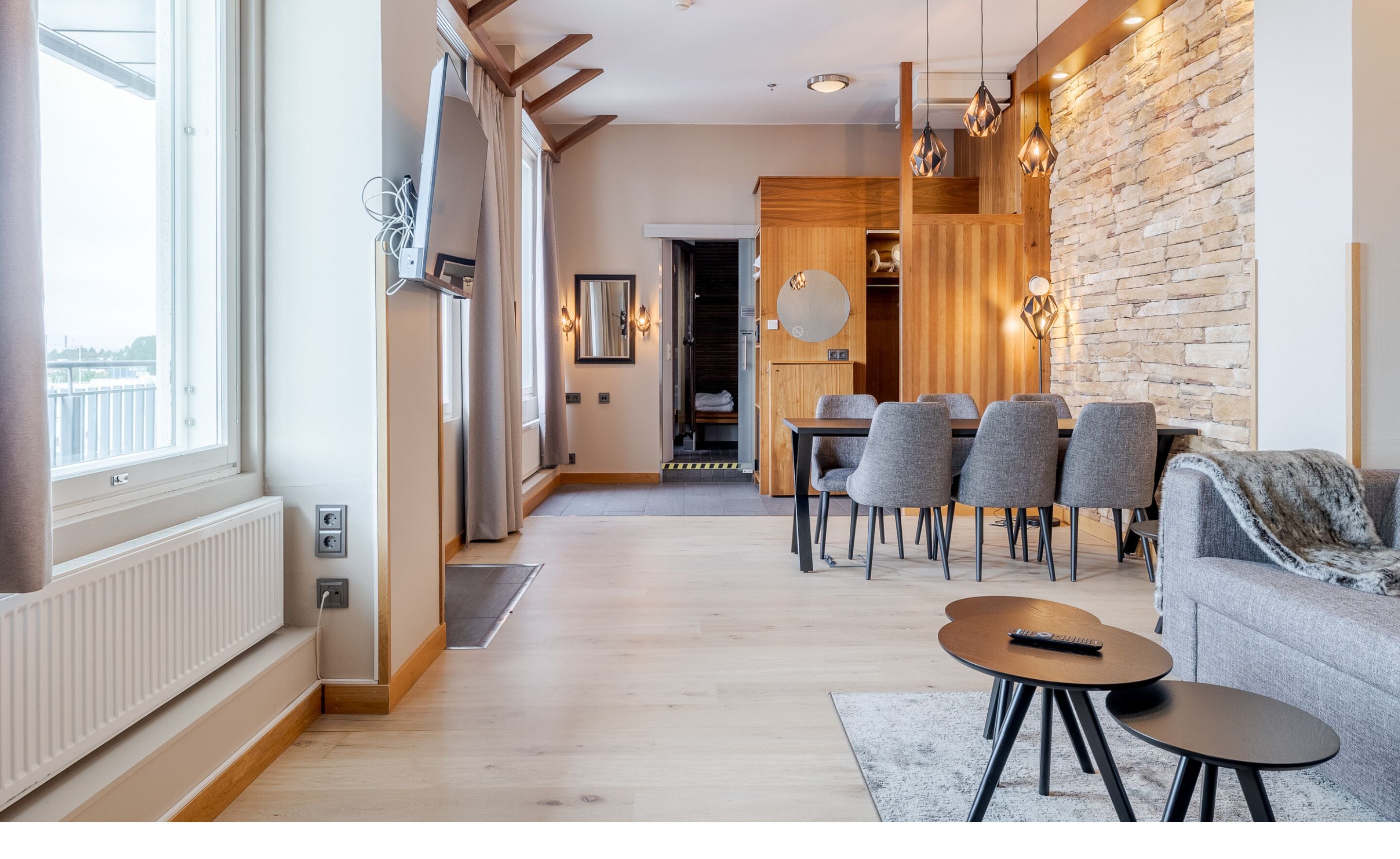 A modern living room with a dining area, wooden accents, and a stone wall.