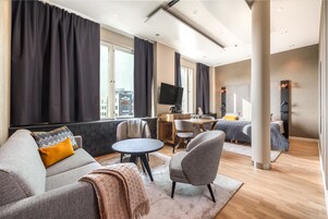 Una habitación de hotel moderna con sofá, sillón, mesa redonda y cama con escritorio.