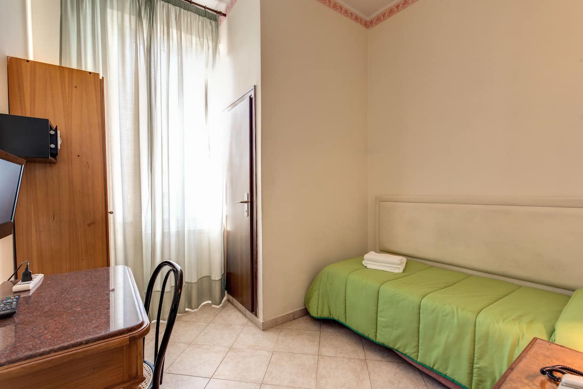 A hotel room with a bed, a desk with a computer, a chair, and a door.