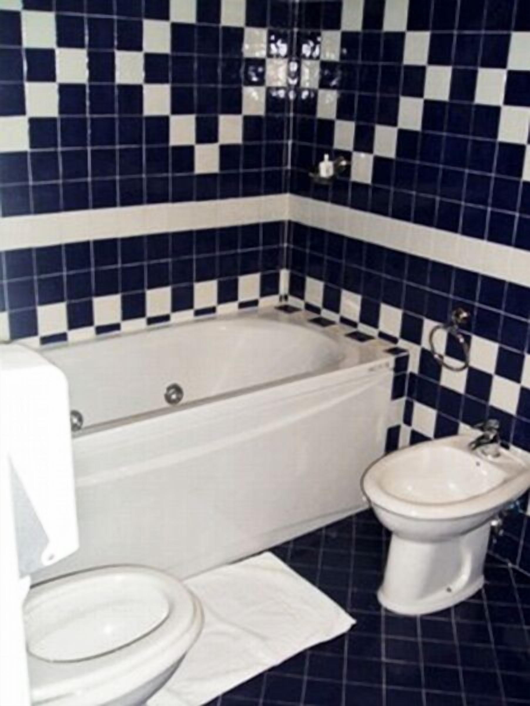 Une salle de bain avec une baignoire blanche, des toilettes blanches et un bidet. Les murs sont recouverts de carreaux bleus et blancs disposés en motif à carreaux.