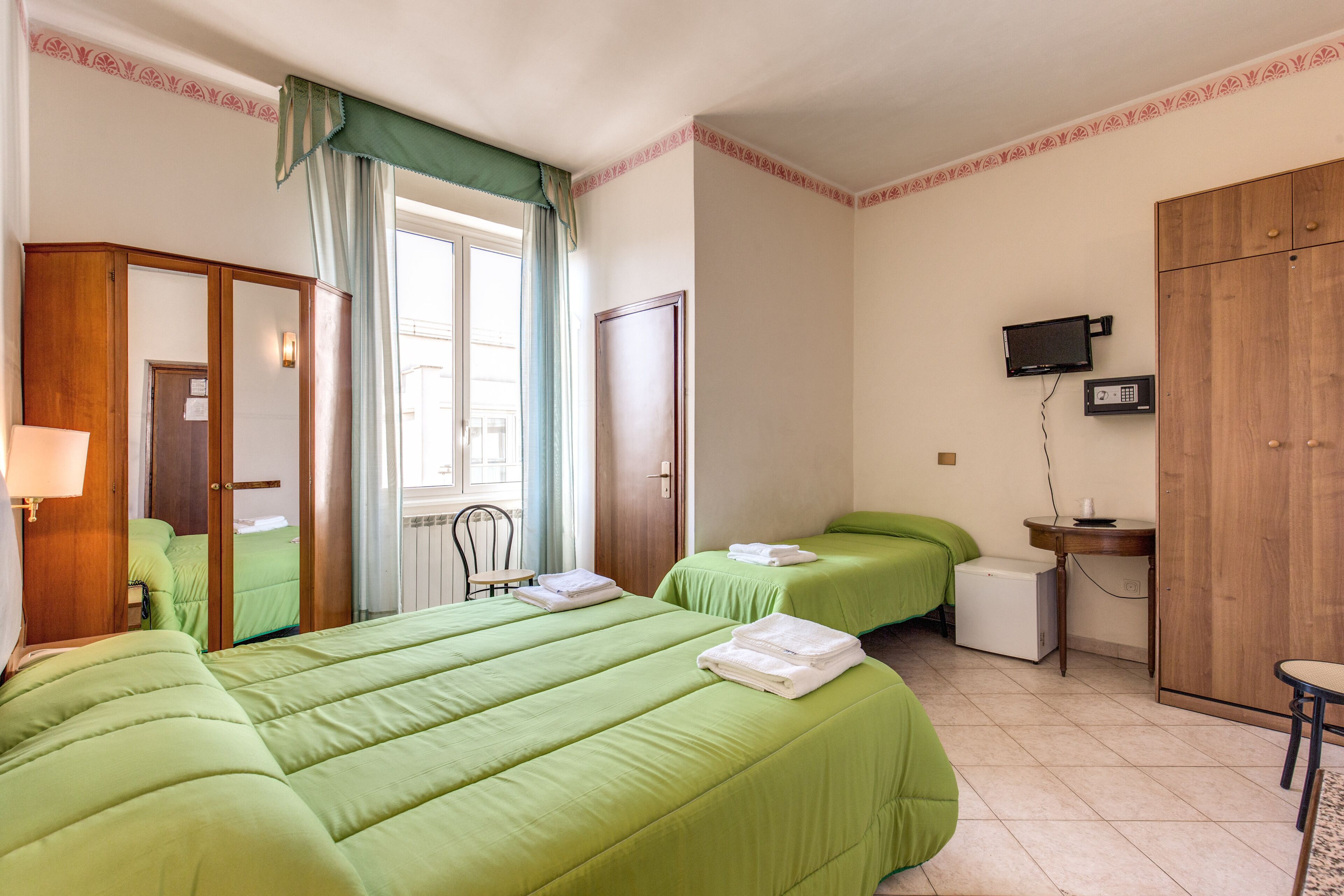 A hotel room with two beds, a desk, a television, and a wardrobe.