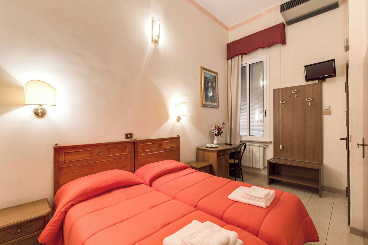 A hotel room with two beds, a desk, a chair, a wardrobe, and a TV.