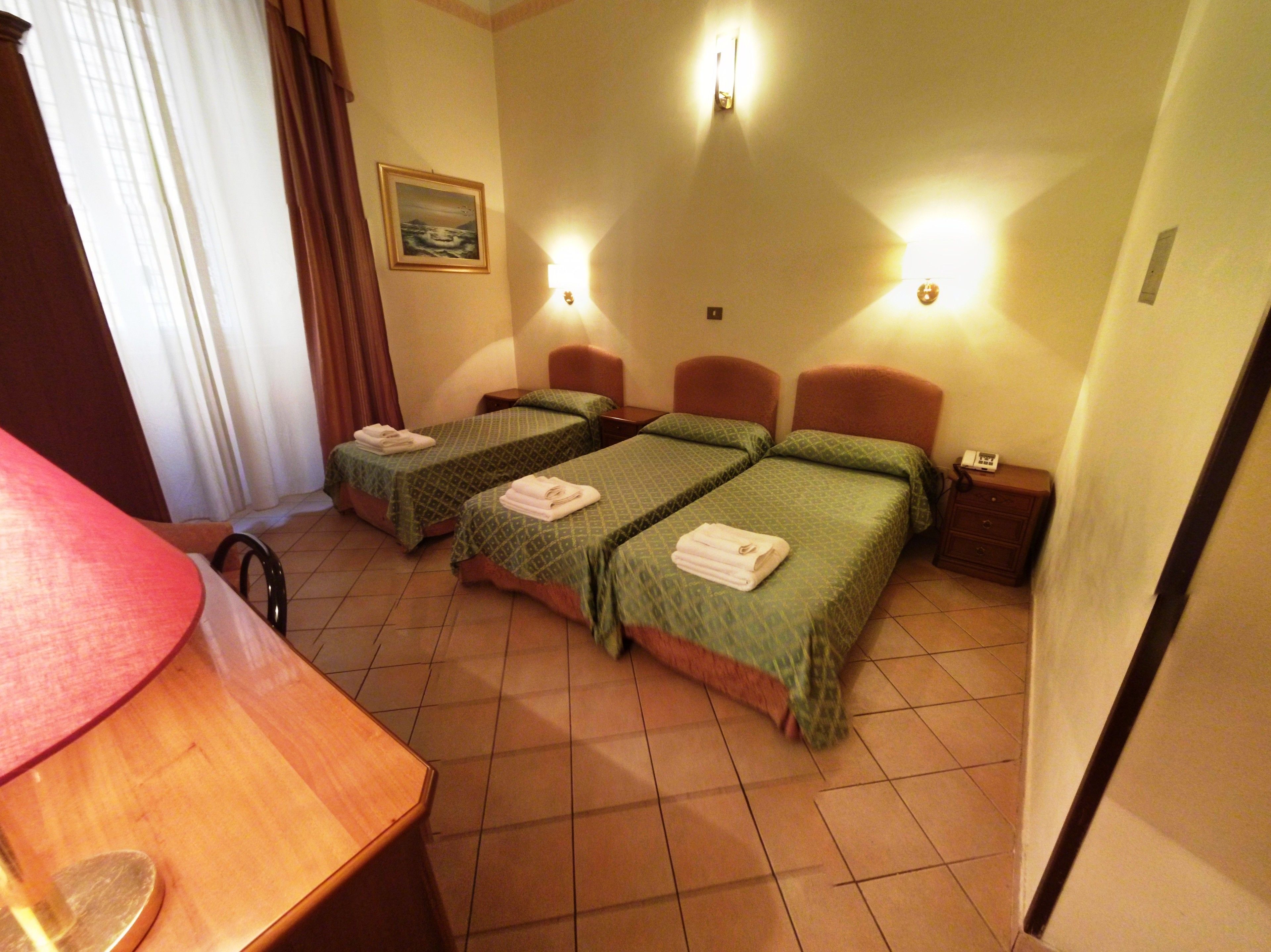 Une chambre d’hôtel avec deux lits, un bureau et une chaise. Il y a deux tables de chevet avec des lampes et un tableau au mur.