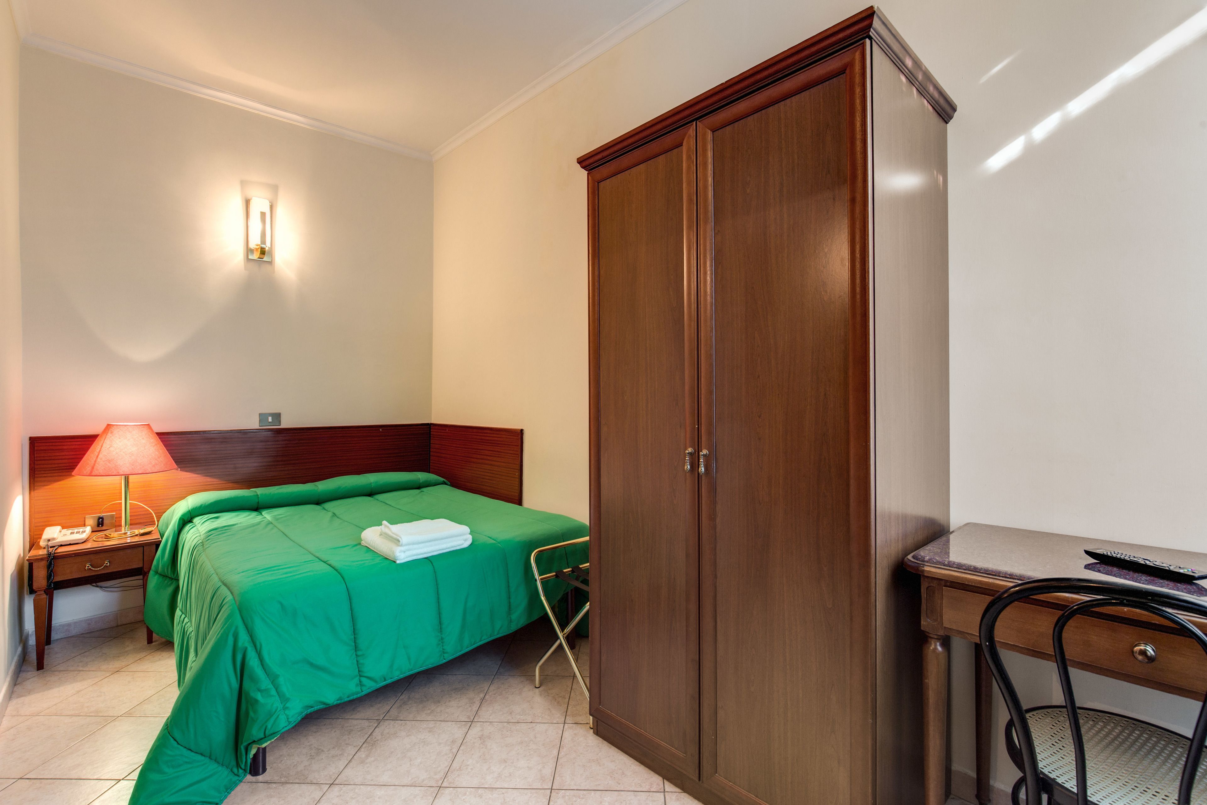 A hotel room with a bed, a wardrobe, a desk, and a chair.