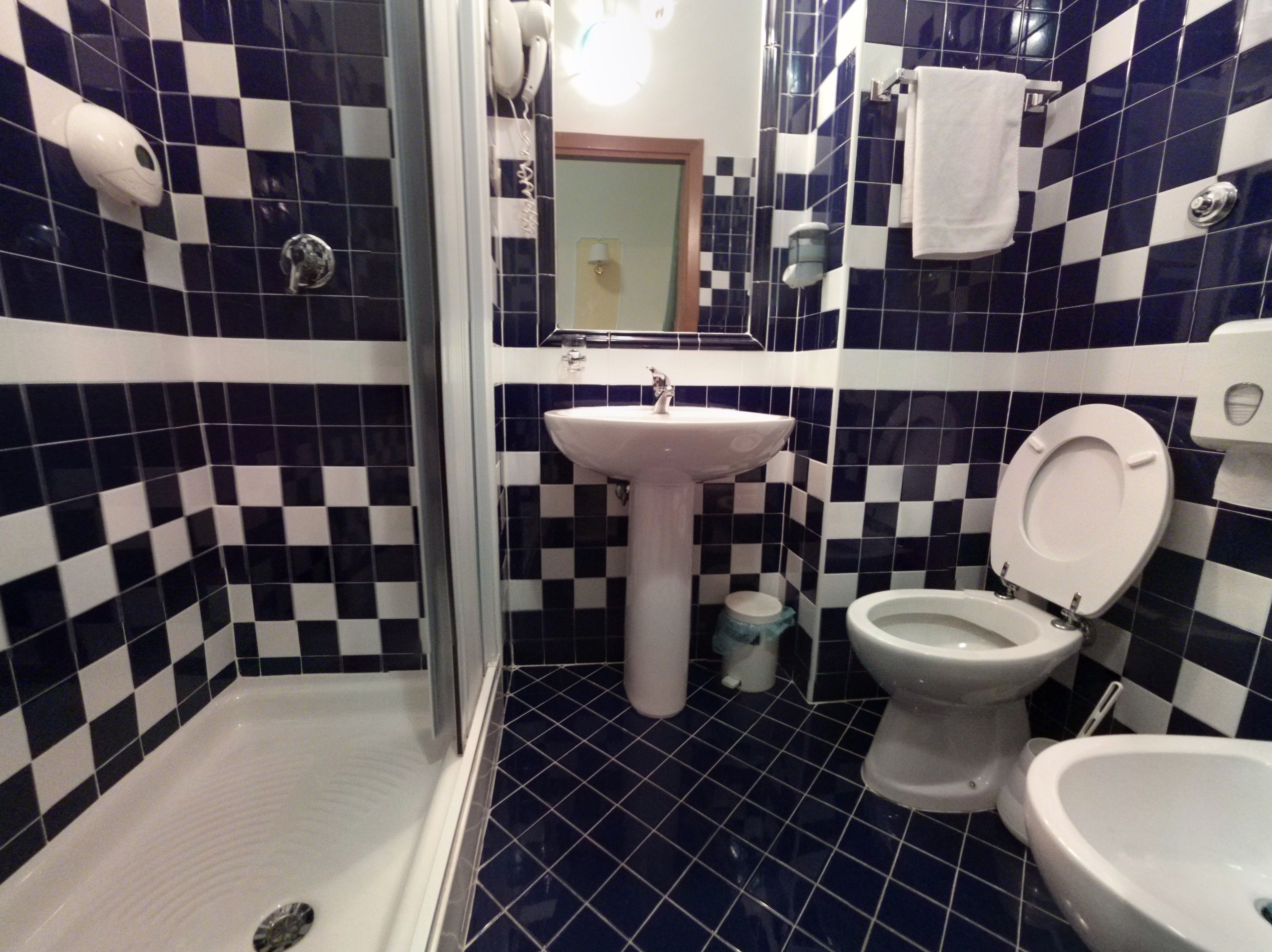A bathroom with a checkered tile pattern, a sink, two toilets, and a shower.