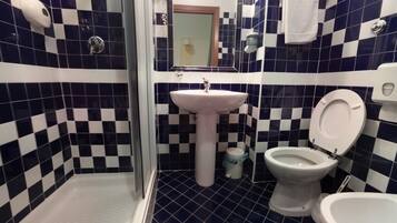 Un baño con piso de baldosas a cuadros, un lavamanos, dos inodoros y una ducha.