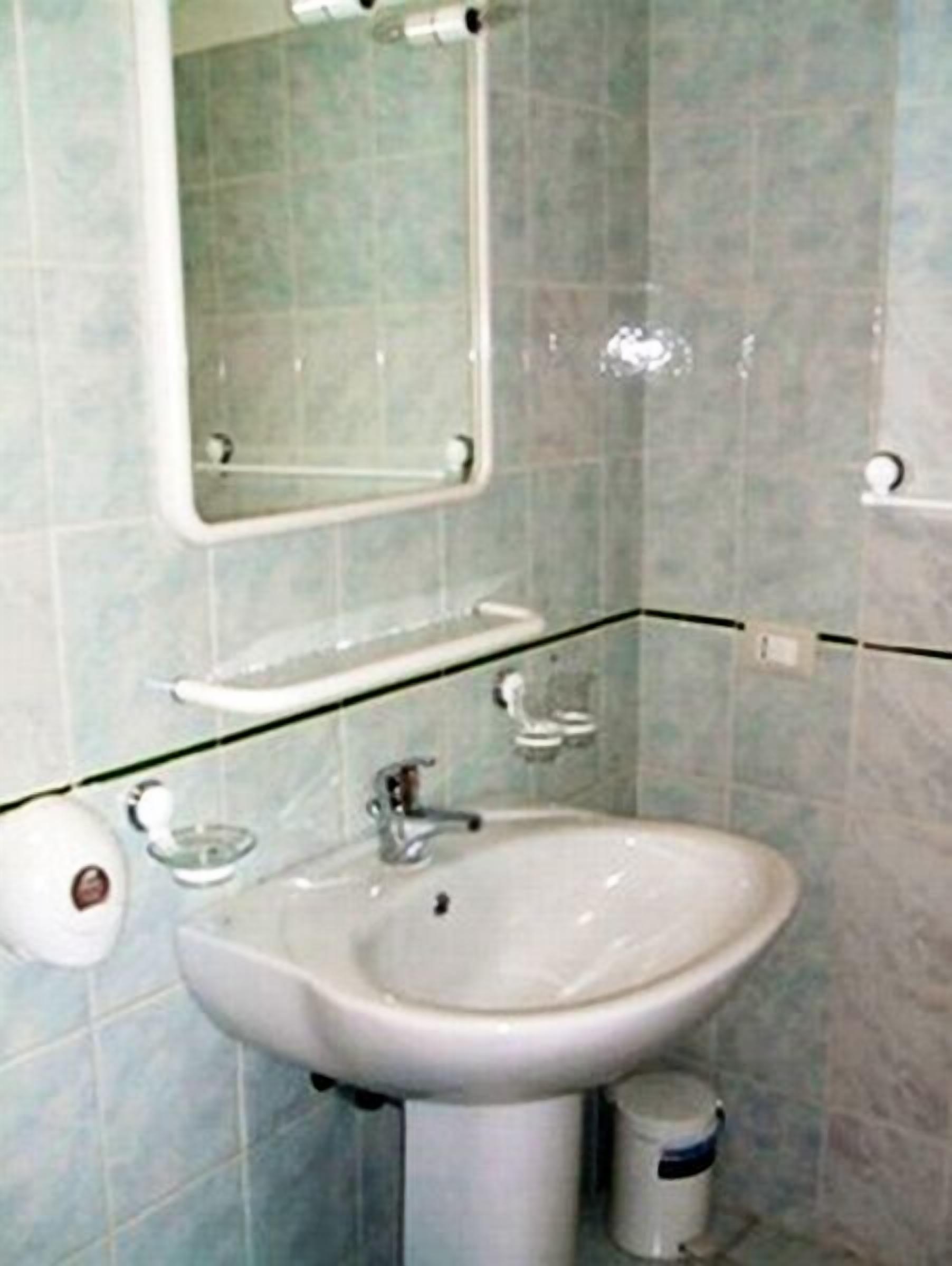 A bathroom with a white sink, a mirror, and a toilet paper holder.
