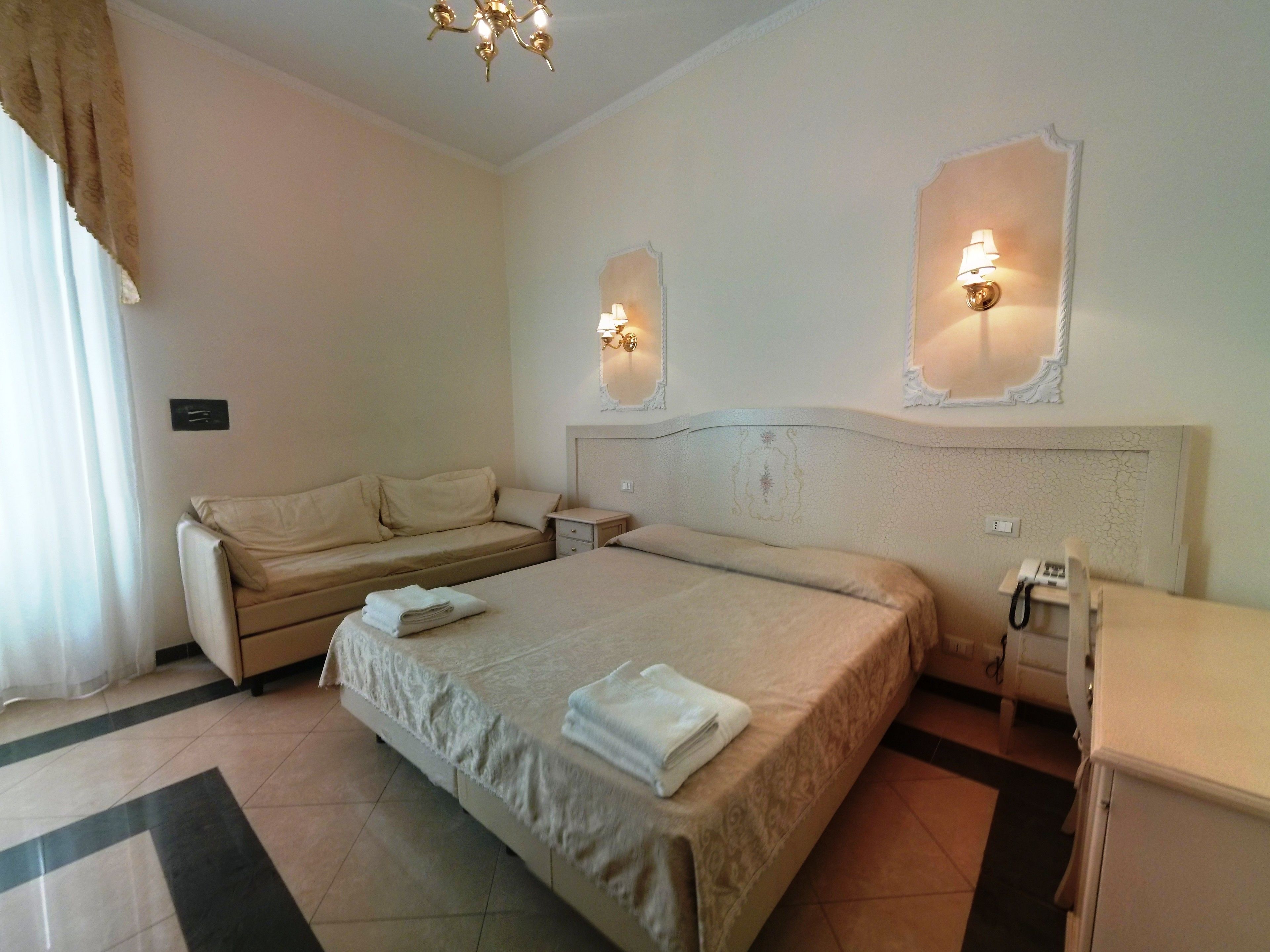 A hotel room with a bed, a sofa, a bedside table, and a telephone.