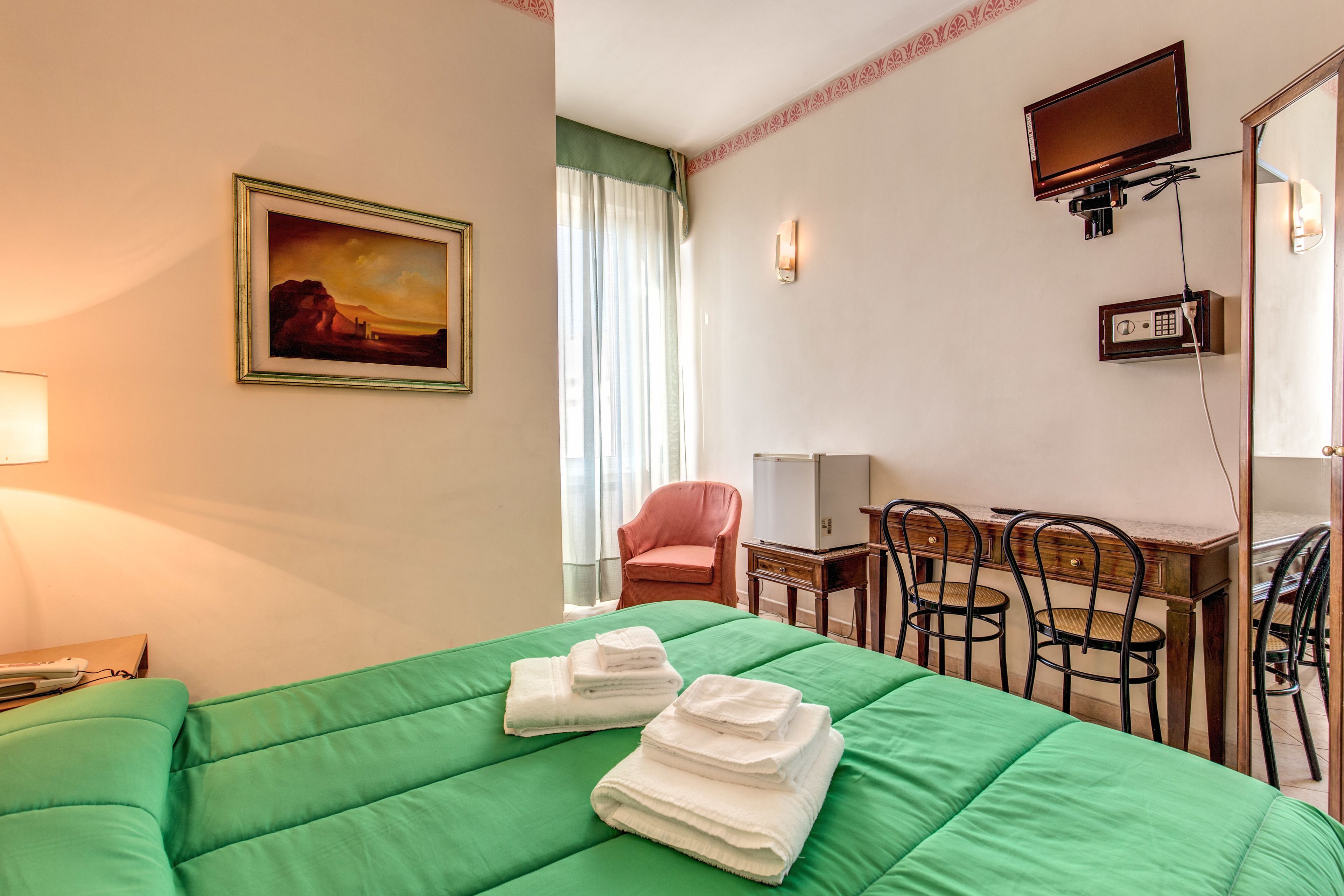 Una habitación de hotel con una cama verde, un escritorio con una silla, un televisor y un cuadro en la pared.
