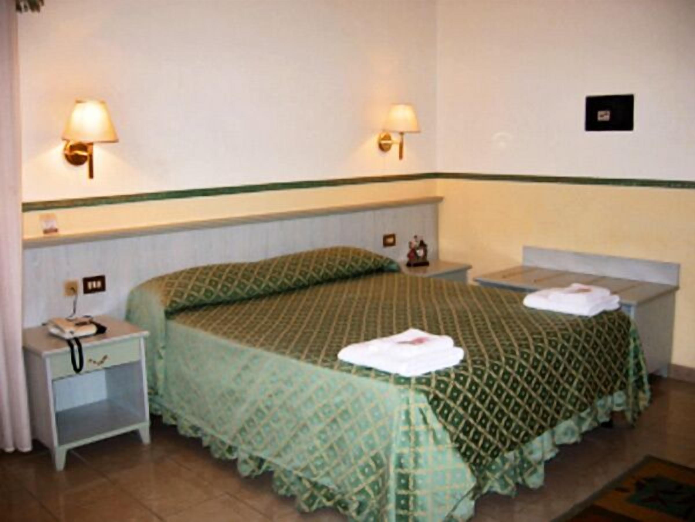 Une chambre d’hôtel comprenant un lit, deux tables de chevet, une petite table et deux lampes fixées au mur.