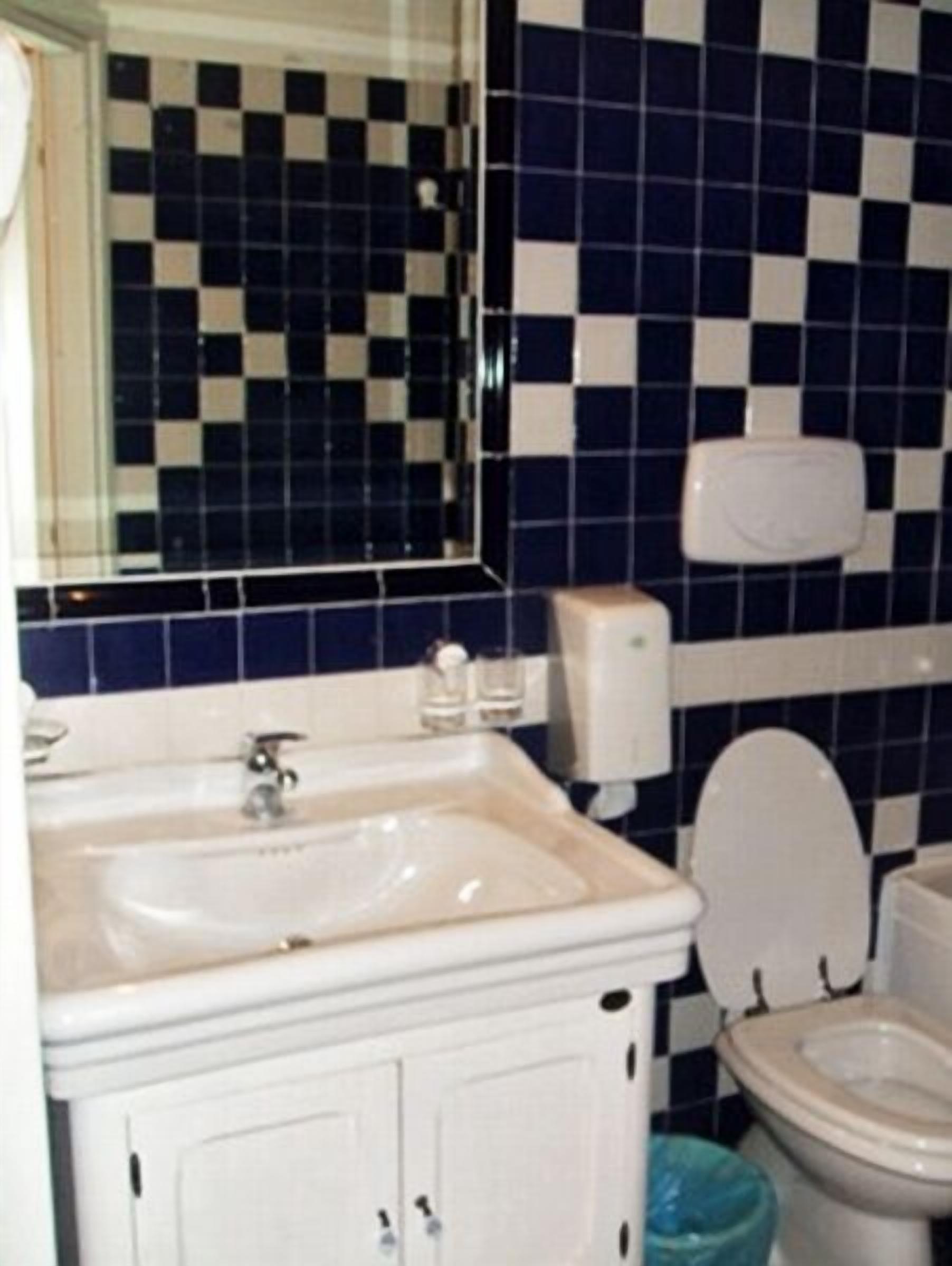 Een badkamer met een wand van zwart-wit betegelde tegels, een wit wastafelmeubel, een toilet en een spiegel.