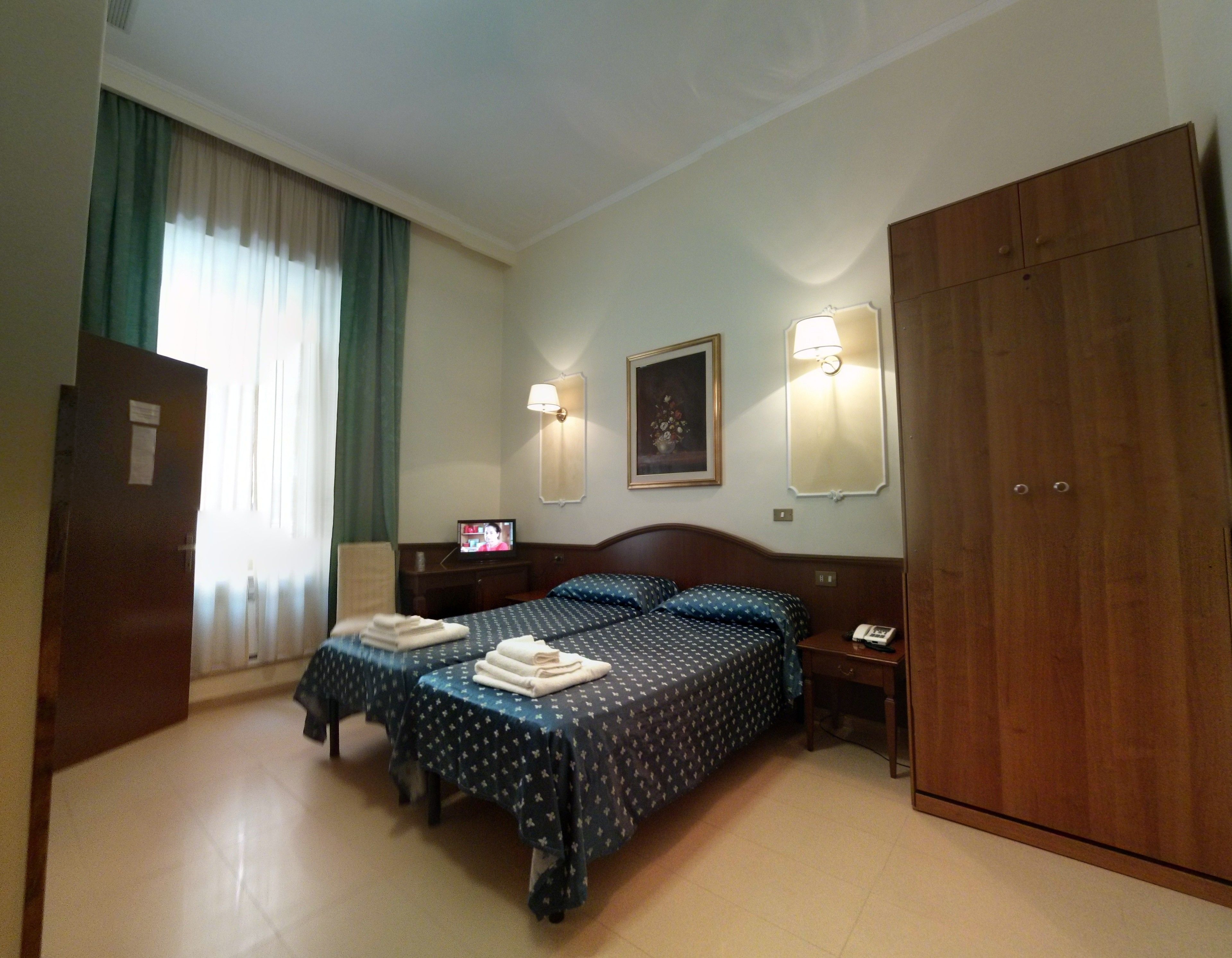 Une chambre d’hôtel avec deux lits, un bureau, une télévision et une armoire.
