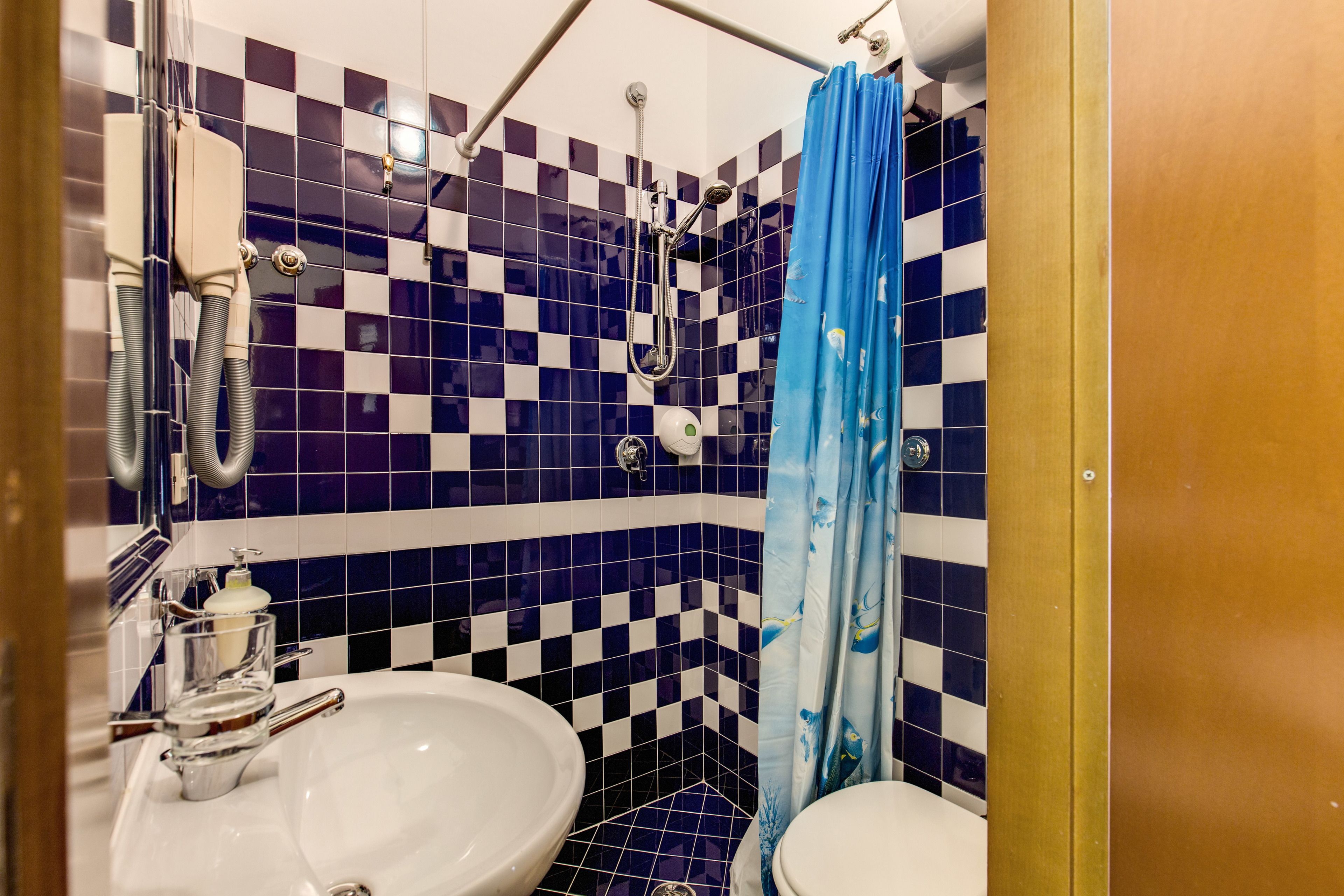 Et badeværelse med væg i skakmønstret fliser, bruser, vask og toilet.