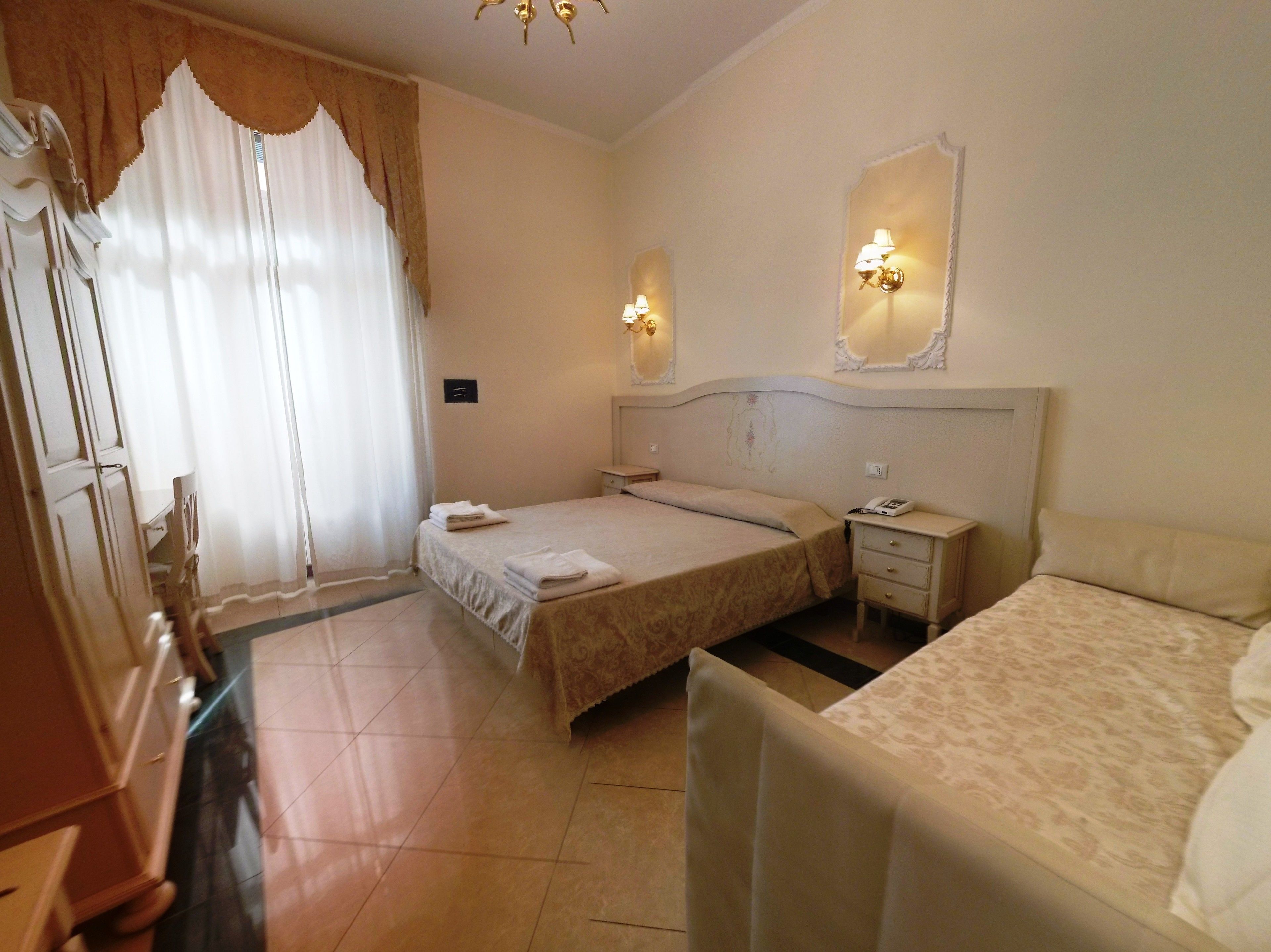 A hotel room with two beds, a nightstand, a mirror, and a window with curtains.