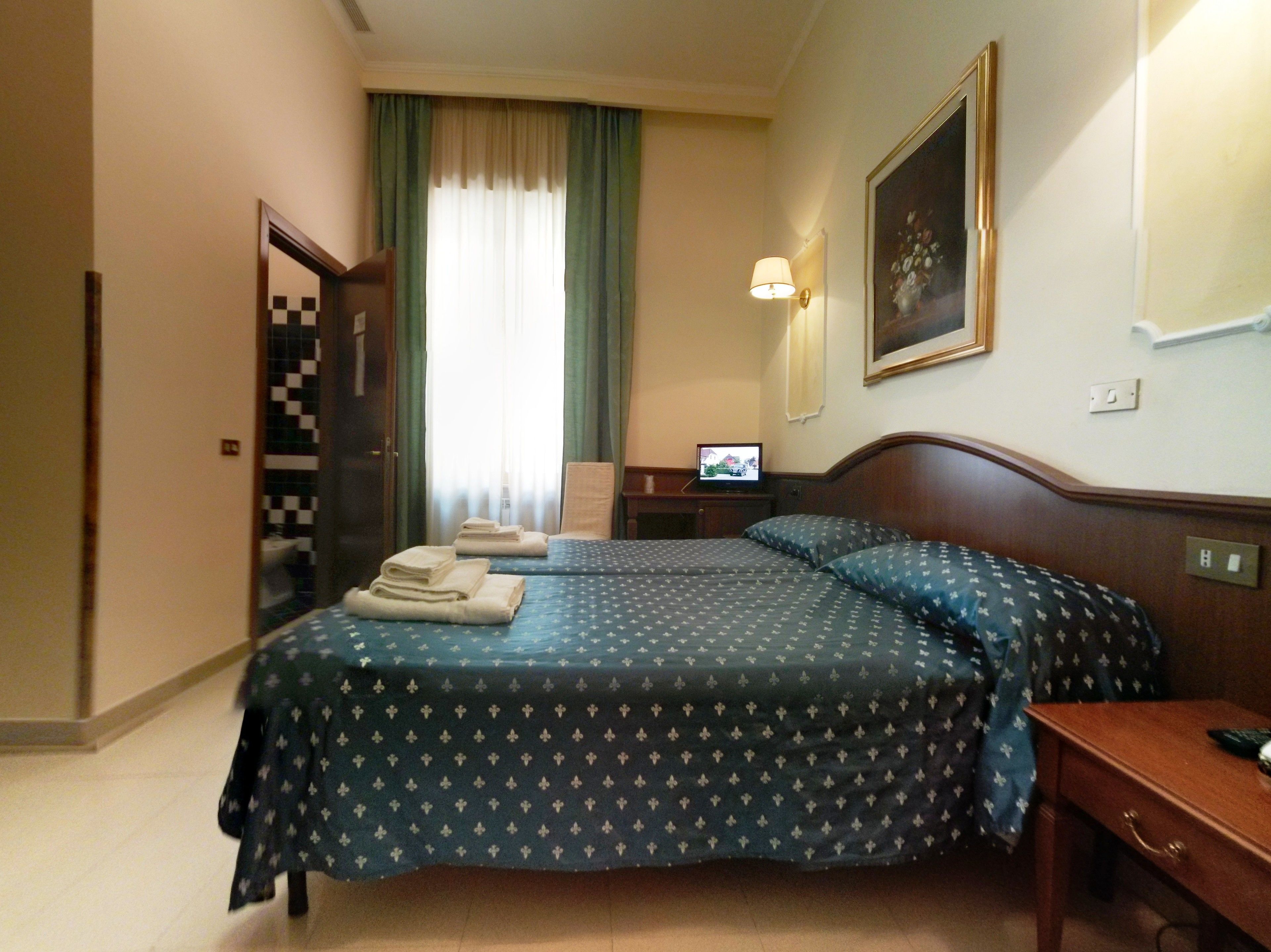 Une chambre d’hôtel avec deux lits, un bureau, une chaise, une télévision et un tableau au mur.