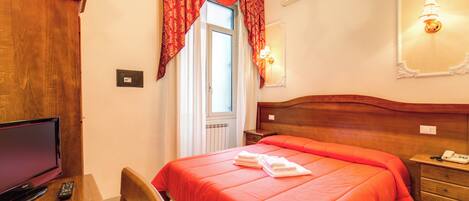 A hotel room with a large bed, a television, a desk with a remote control, and a window with curtains.