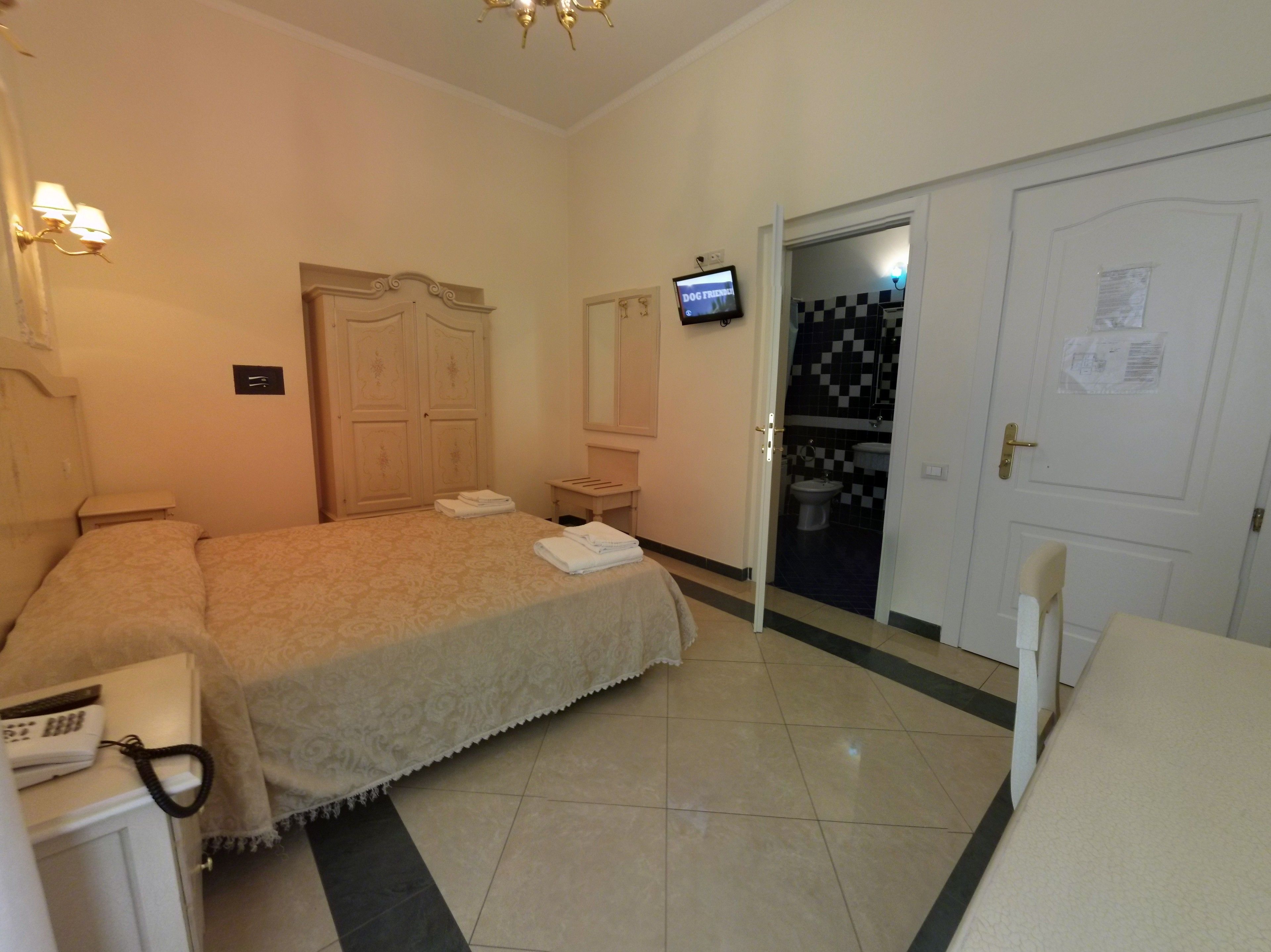 A hotel room with a bed, a desk, a chair, a TV, and a bathroom visible through an open door.