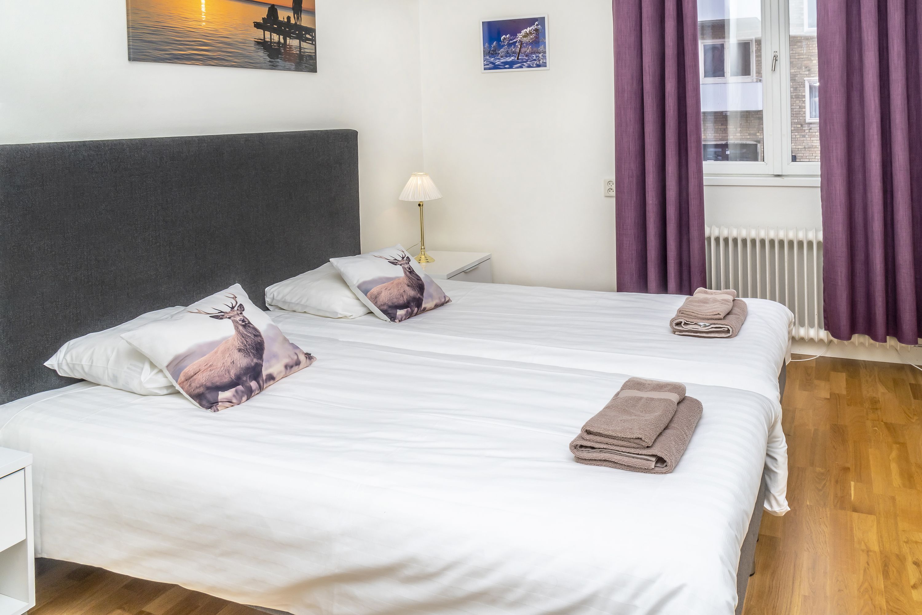 A double bed with white linens, two pillows with deer prints, and a folded towel on the side.