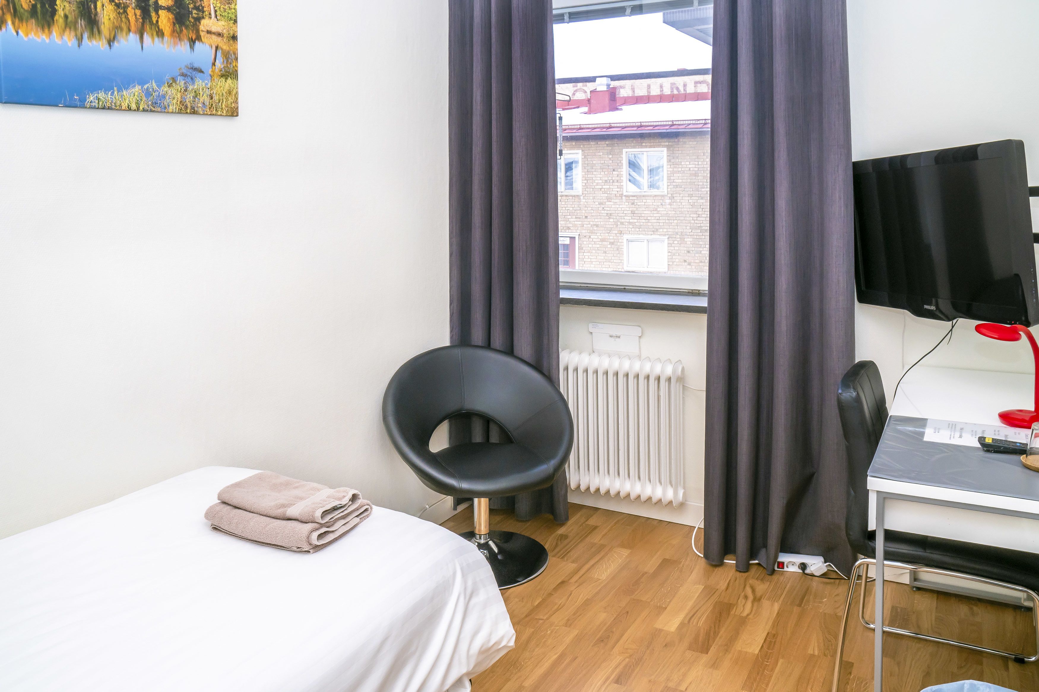 A hotel room with a bed, a chair, a desk with a computer, a TV, and a window with curtains.