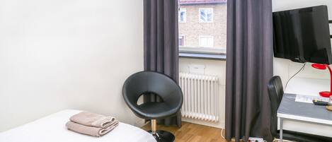 A hotel room with a bed, a chair, a desk with a computer, a TV, and a window with curtains.