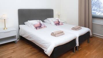 A neatly made double bed with white linens and two pillows featuring a deer design, a bedside table with a lamp, and a window with a view of a snowy landscape.