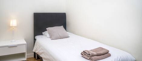 A neatly made bed with a pillow and a folded towel, a bedside lamp, and a small nightstand.