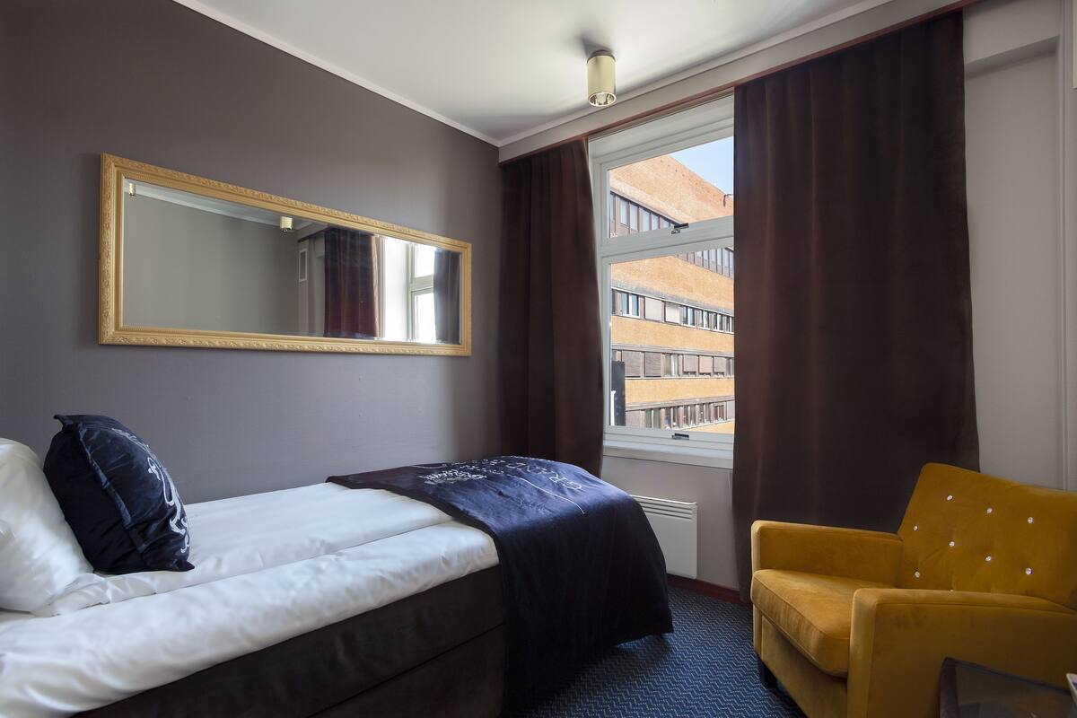 Habitación de hotel con cama, una silla, un espejo grande y una ventana con cortinas.