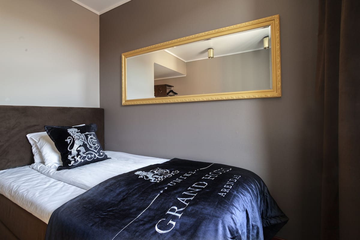 Habitación de hotel con cama, un espejo grande y una colcha azul oscuro con texto.
