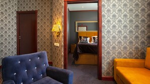 A hotel room with a bed, a blue armchair, a yellow sofa, and patterned wallpaper. - Grand Hotel Arendal - Unike Hoteller (Arendal)
