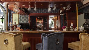 A bar area with a wooden sign reading "GRAND BAR," bar stools, and a wine rack with glasses. - Grand Hotel Arendal - Unike Hoteller (Arendal)