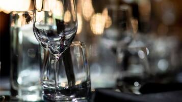 A table set with clear glassware, including a wine glass and a water glass, in a dimly lit setting with blurred background lights.