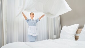A hotel room with a neatly made bed, a bedside table with a lamp, and sheer curtains. - Grand Hotel Arendal - Unike Hoteller (Arendal)